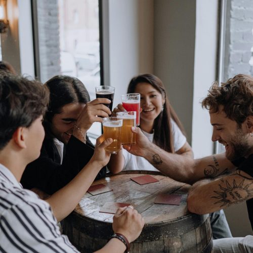 Young adults toasting with beer at a cozy bar setting, enjoying time together.